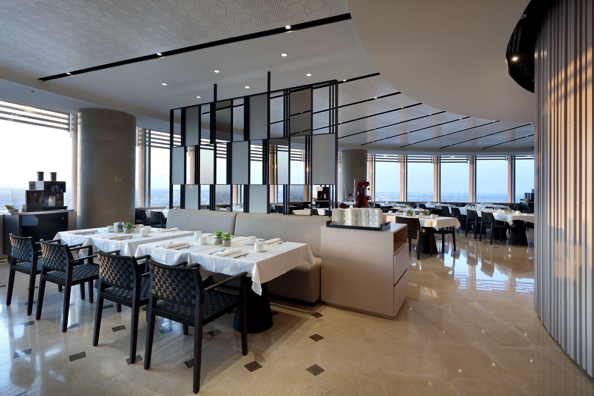 Eurostars Torre Sevilla Exterior foto The photo shows the interior of a modern restaurant. The design features a curved layout with elegant decor. There are several tables set with white tablecloths and black chairs. Large windows provide a view of the outside, allowing natural light to 