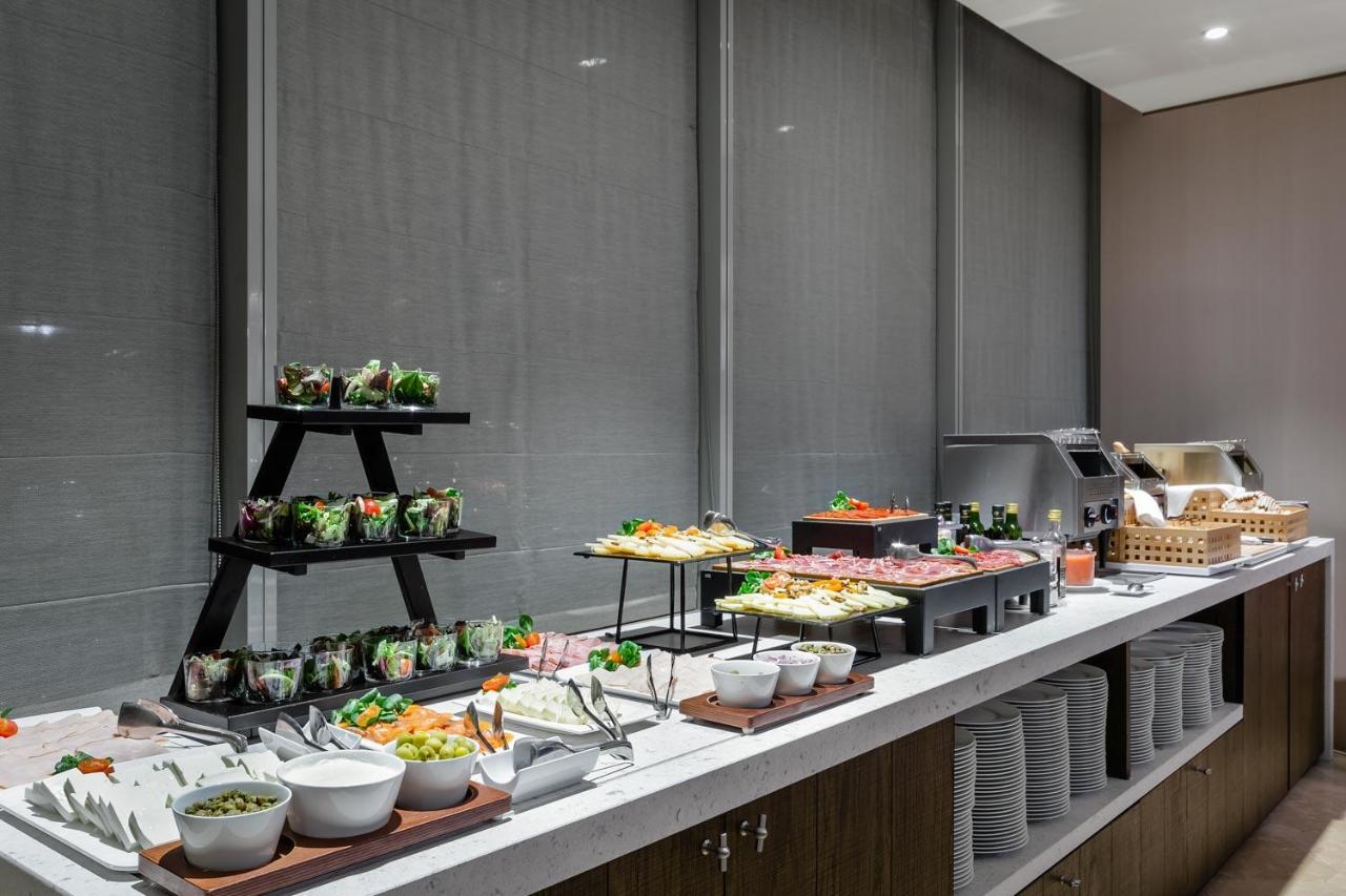 Eurostars Torre Sevilla Exterior foto The photo shows a buffet-style food display. There's a long countertop with various dishes arranged neatly. On the left, there are several small bowls and containers with salads, possibly garnished with fresh vegetables. In the center, there appears 