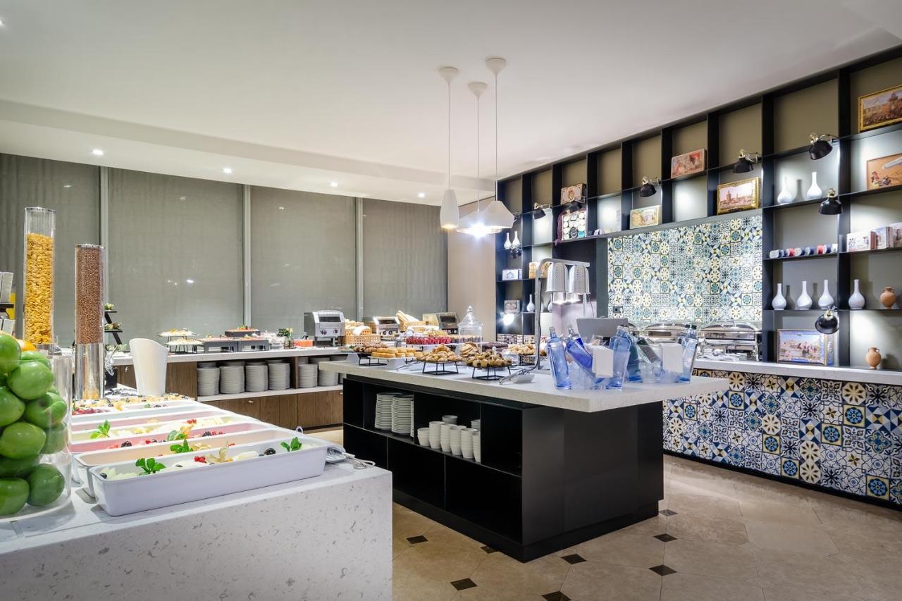 Eurostars Torre Sevilla Exterior foto The photo shows a modern buffet or dining area with a sleek design. There are multiple food stations, featuring a variety of dishes displayed on long tables. One table has bright, fresh-looking salads and ingredients, while another showcases desserts