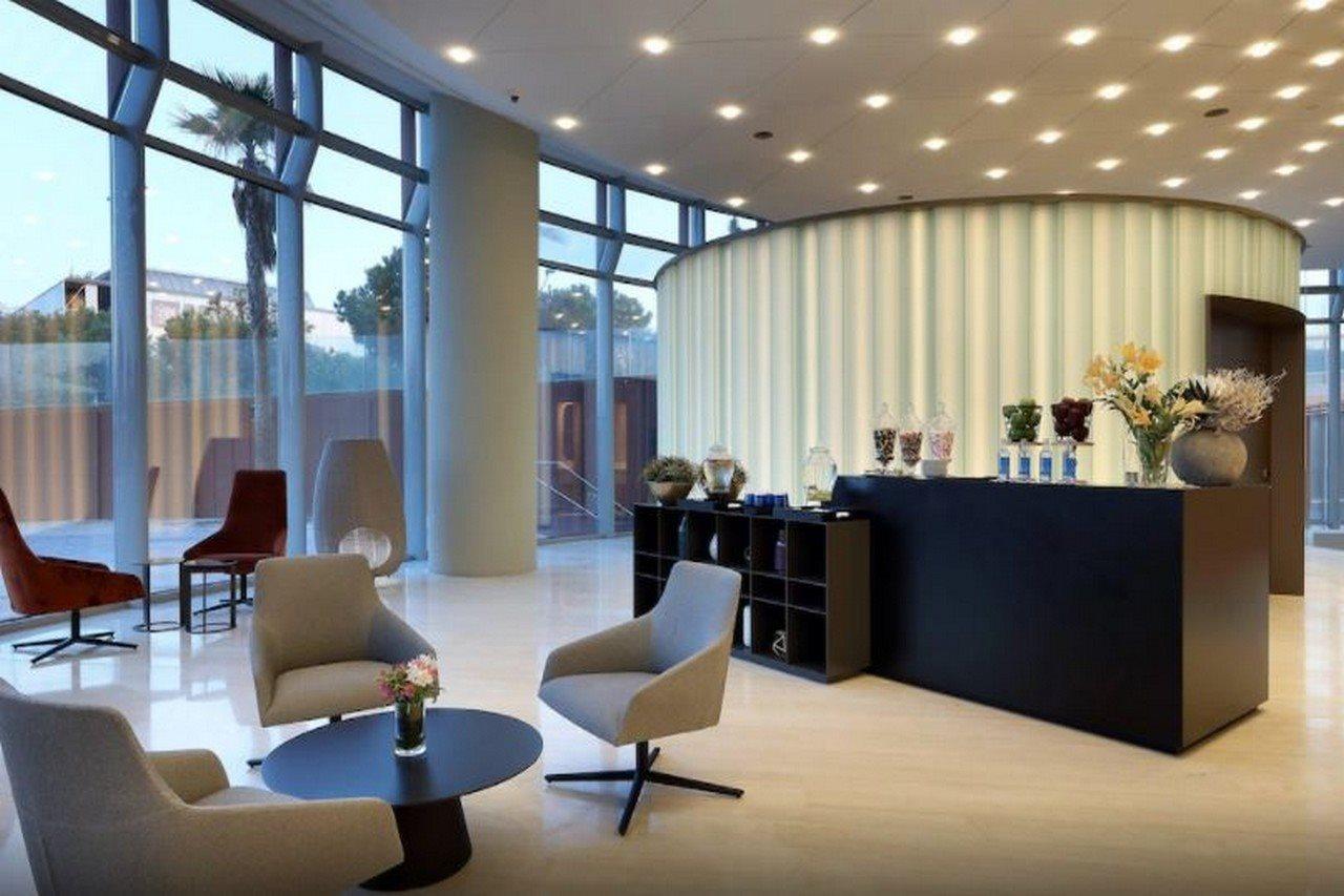 Eurostars Torre Sevilla Exterior foto The photo shows a modern reception area or lobby. It features large windows that let in natural light, creating a bright and inviting atmosphere. The interior design includes a mix of seating options, such as grey armchairs and a small black coffee t