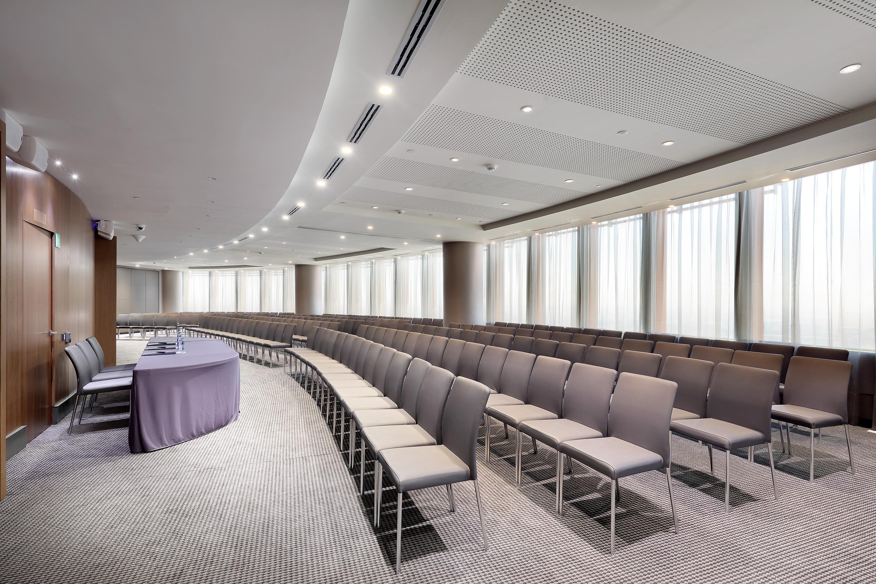Eurostars Torre Sevilla Exterior foto The photo shows a conference room or meeting space designed for presentations or gatherings. There are rows of grey chairs arranged in a semi-circular layout, indicating a focus on a speaker or presentation area. At the front of the room, there is a 
