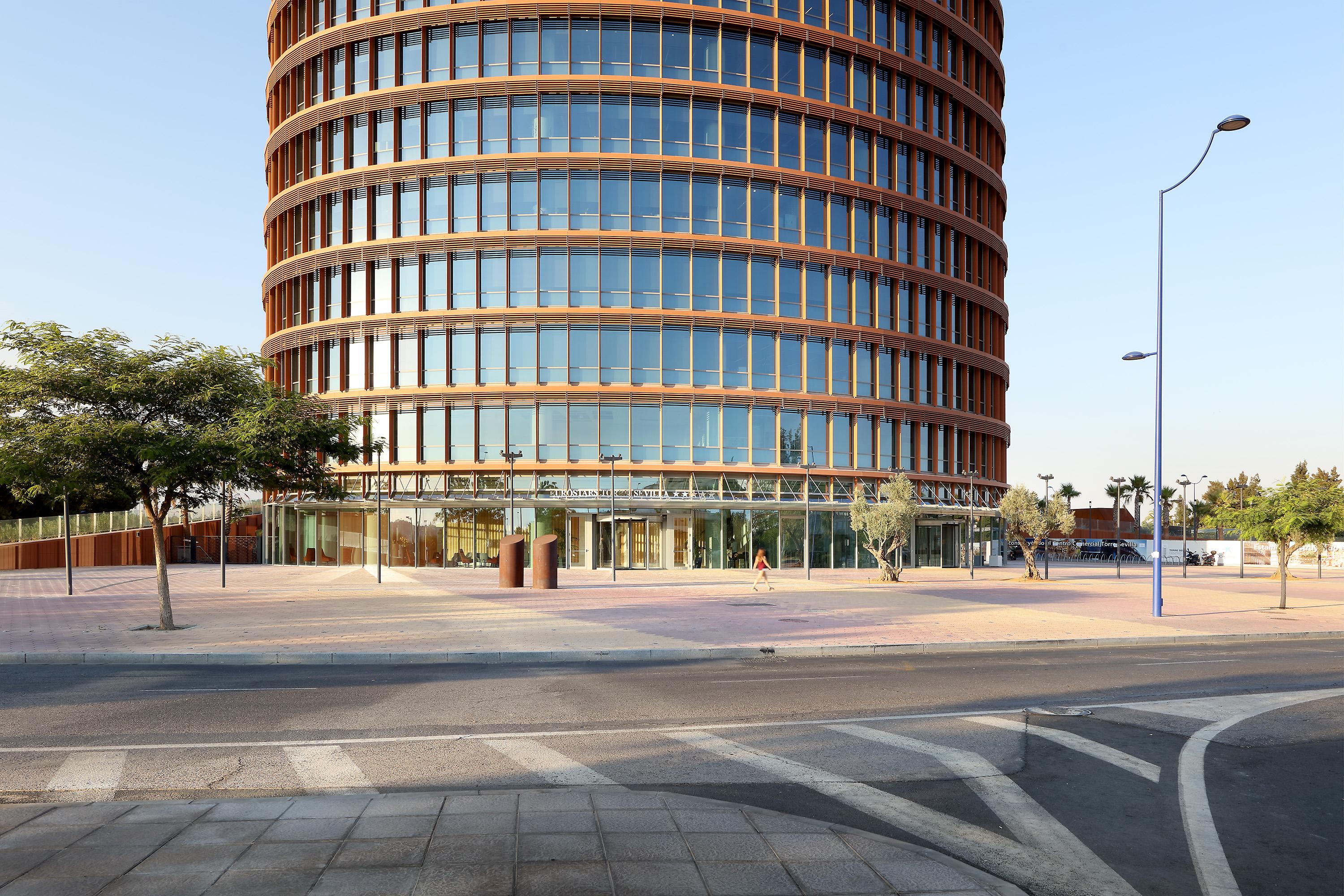 Eurostars Torre Sevilla Exterior foto The photo depicts a modern, multi-story building characterized by its round shape and large glass windows. The facade features a combination of glass and wood elements, giving it a sleek and contemporary appearance. In the foreground, there is an ope