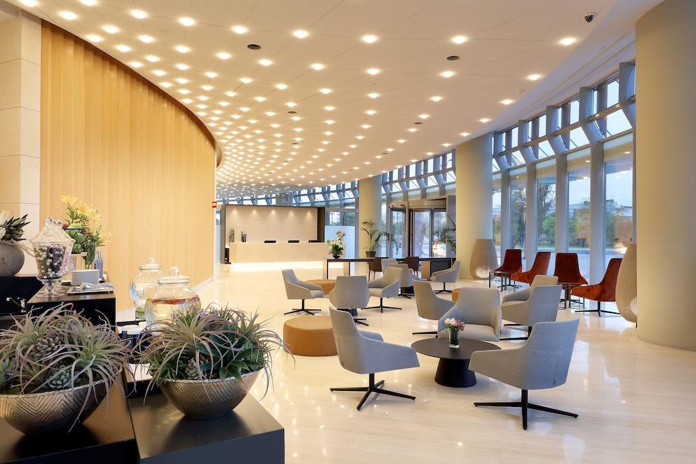 Eurostars Torre Sevilla Exterior foto The photo shows a modern, well-lit lobby or lounge area. The design features smooth lines and a contemporary aesthetic, with a curved wooden wall and large windows allowing natural light to fill the space. There are stylish seating arrangements, incl