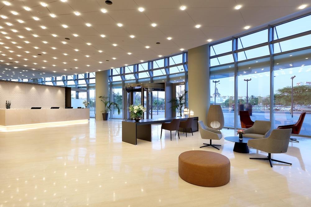 Eurostars Torre Sevilla Exterior foto The image depicts a modern reception area or lobby of a building. It features high ceilings and large windows that allow natural light to flood the space. The floor is polished and likely made of marble or a similar material, giving it a sleek appear