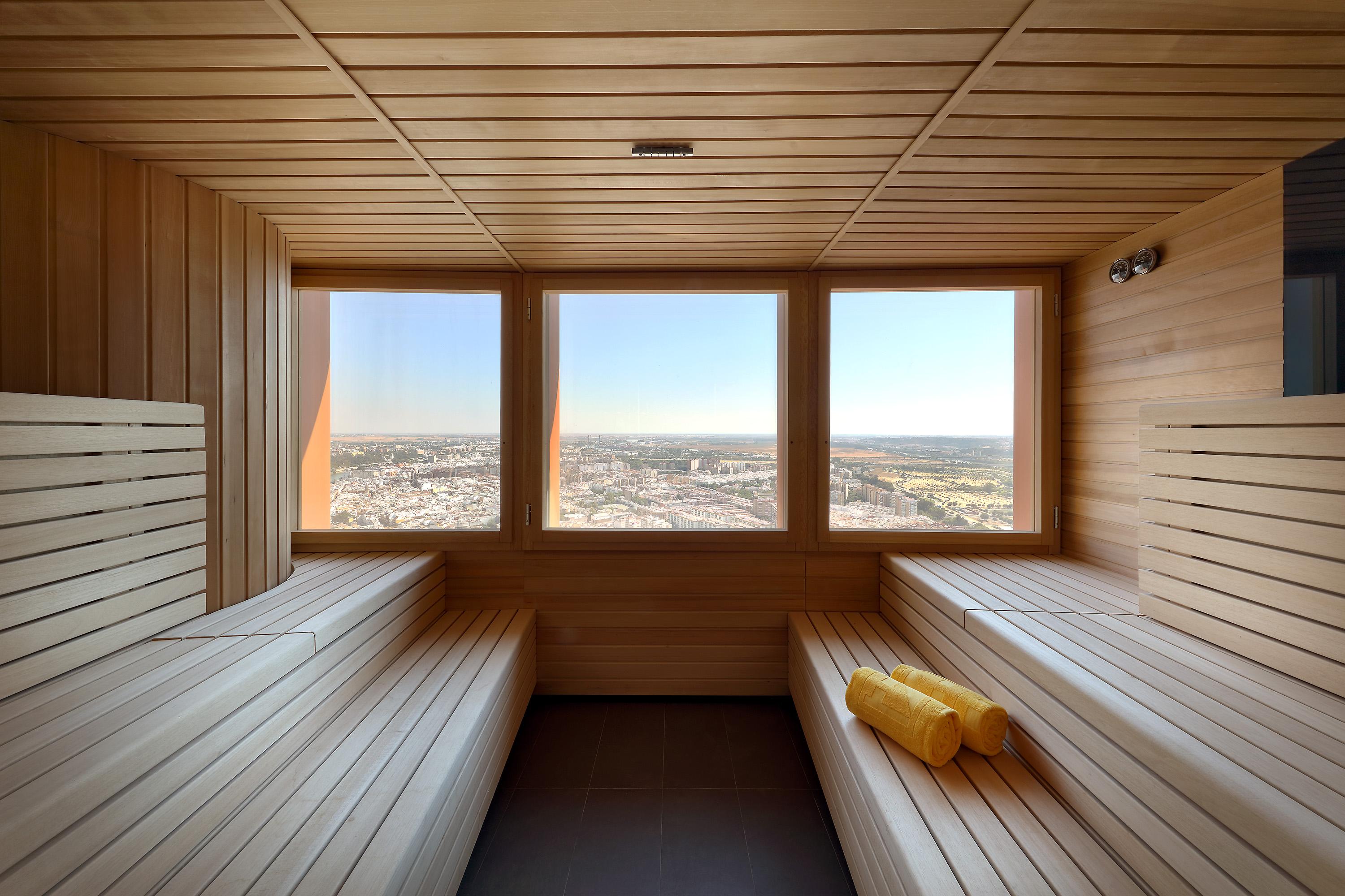Eurostars Torre Sevilla Exterior foto The photo shows the interior of a sauna made primarily of wood. It features wooden benches arranged in a tiered setup, allowing for seating at different heights. There are large windows that provide a panoramic view of the outside landscape, showcasi