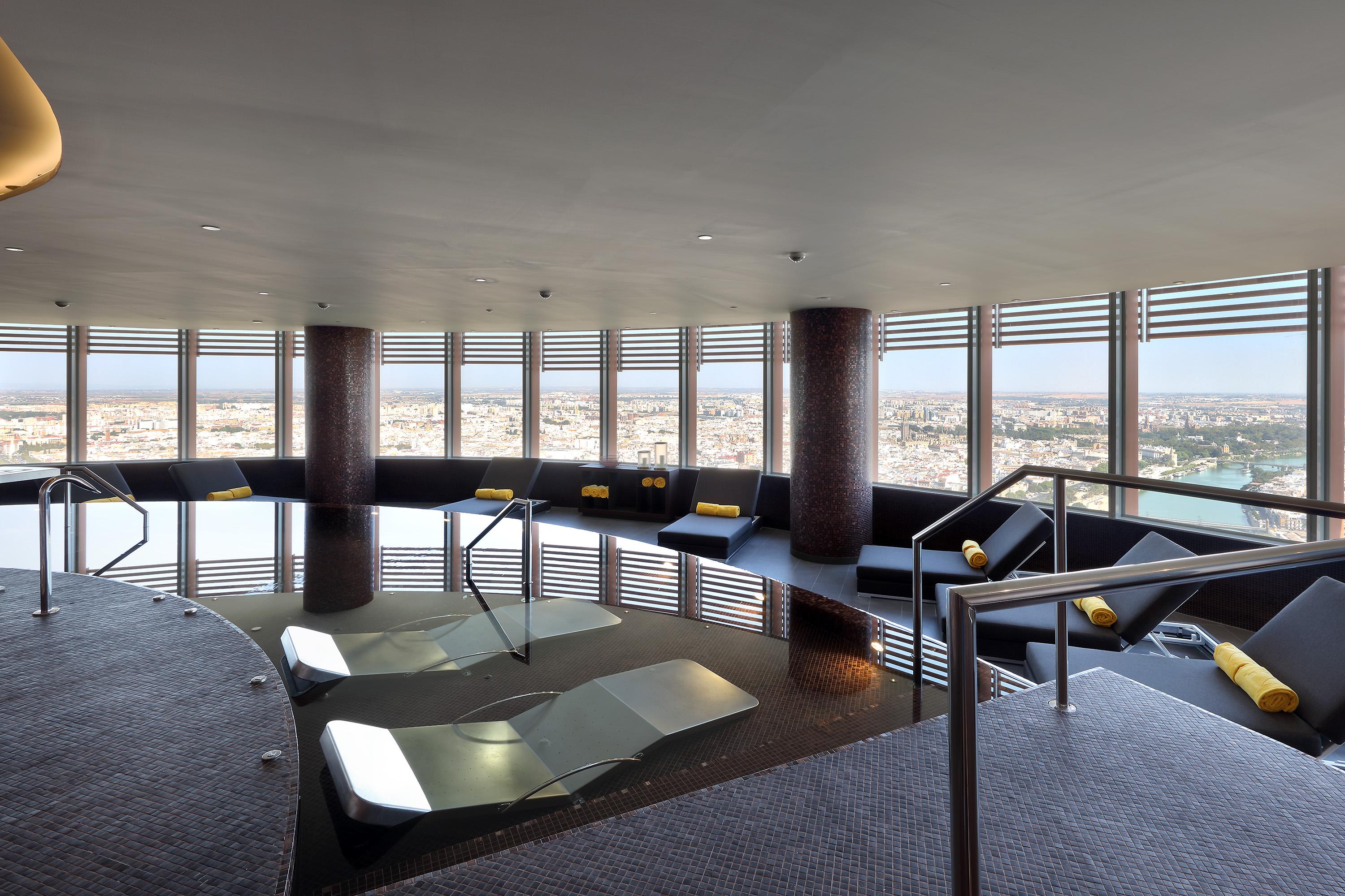 Eurostars Torre Sevilla Exterior foto The photo depicts an elegant spa or wellness area with a large, circular pool surrounded by comfortable seating. The space features large windows that offer a panoramic view of the city outside, allowing natural light to illuminate the room. The inte