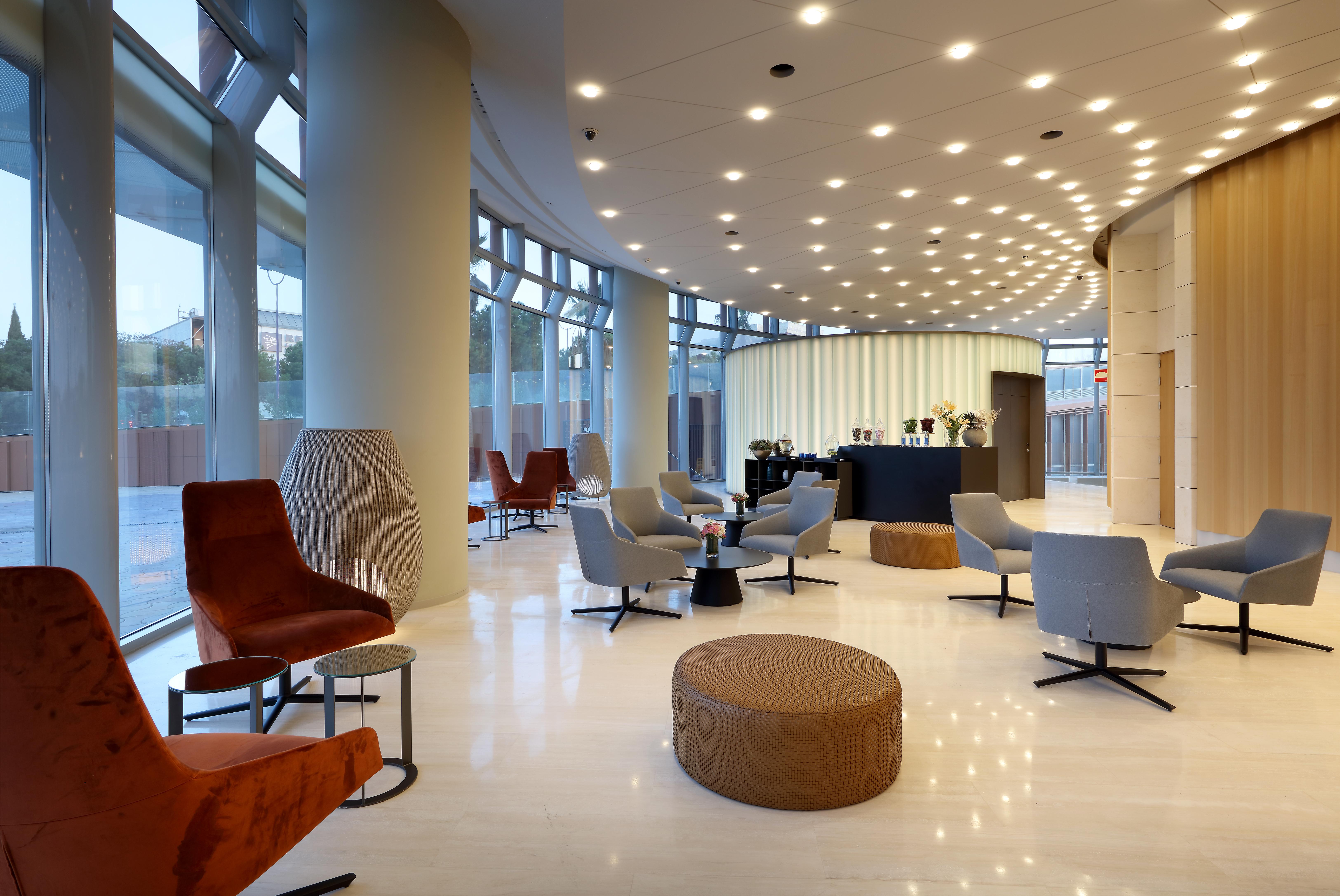 Eurostars Torre Sevilla Exterior foto The photo shows a modern, stylish lobby or lounge area. The design features a curved layout with large windows allowing natural light to flood the space. Various seating options are arranged throughout, including a mix of armchairs, lounge chairs, an