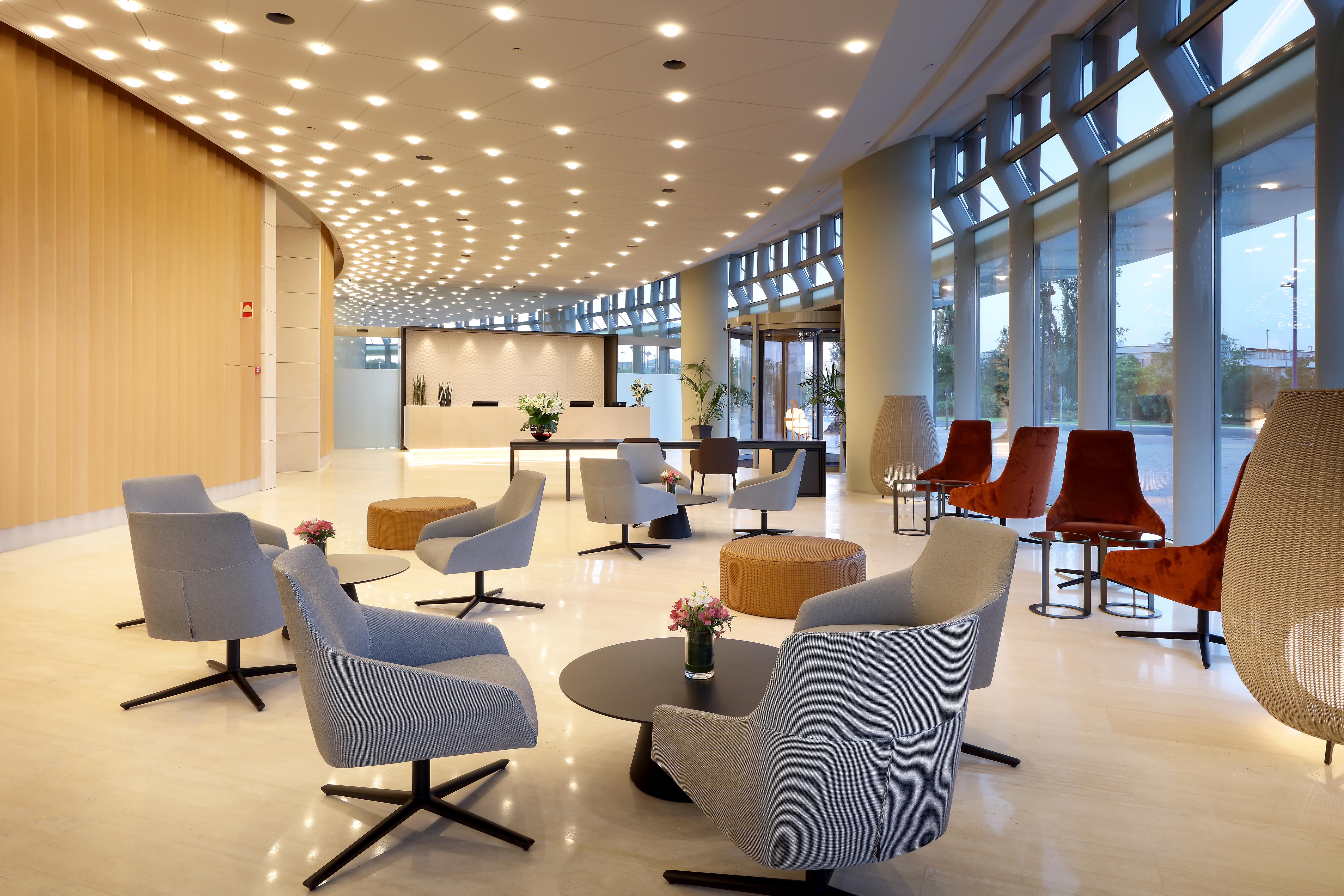 Eurostars Torre Sevilla Exterior foto The photo shows a modern lobby or reception area. It features a sleek design with a combination of chairs and tables arranged in a welcoming manner. The seating includes soft, light-colored armchairs and some darker, stylized chairs. In the center, t