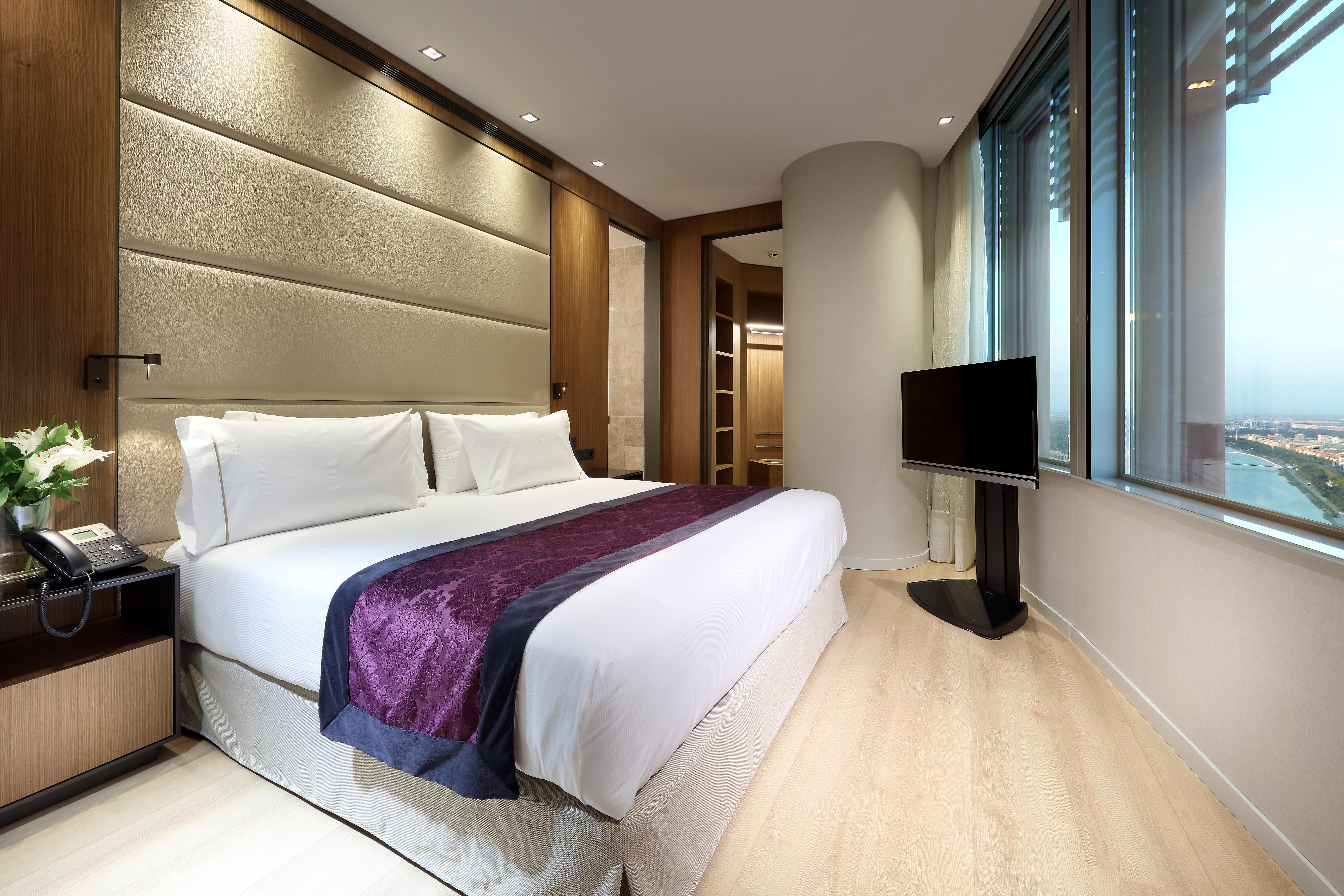 Eurostars Torre Sevilla Exterior foto The photo showcases a modern hotel room featuring a king-sized bed with white linens and a decorative purple accent. The room has wooden flooring and is well-lit with recessed lighting. Behind the bed, there is a plush headboard with a textured desig