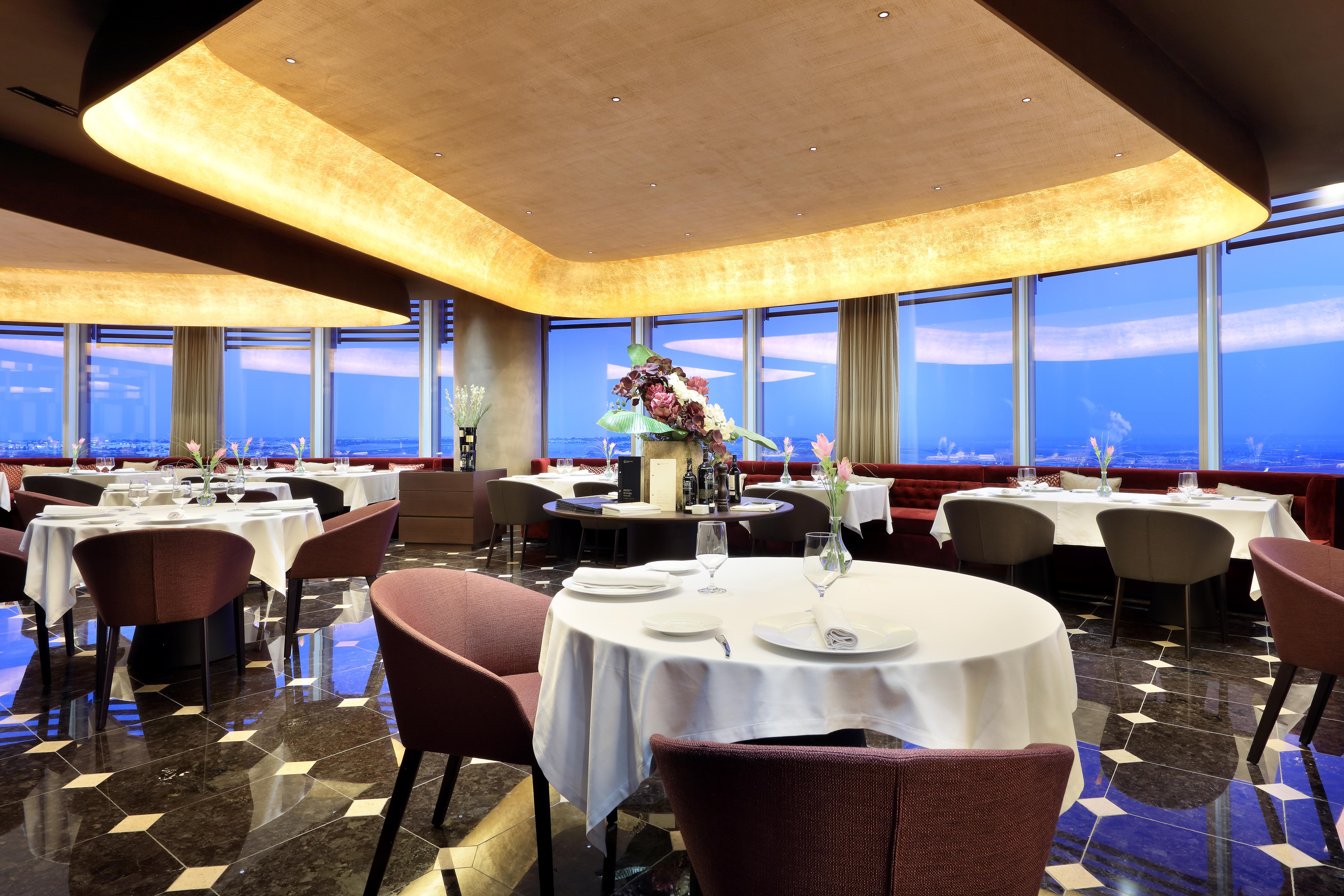 Eurostars Torre Sevilla Exterior foto The photo shows an elegant restaurant interior with a modern design. There are several round tables, each set with white tablecloths and place settings, including glasses and dishes. The seating consists of plush chairs that appear comfortable. The r