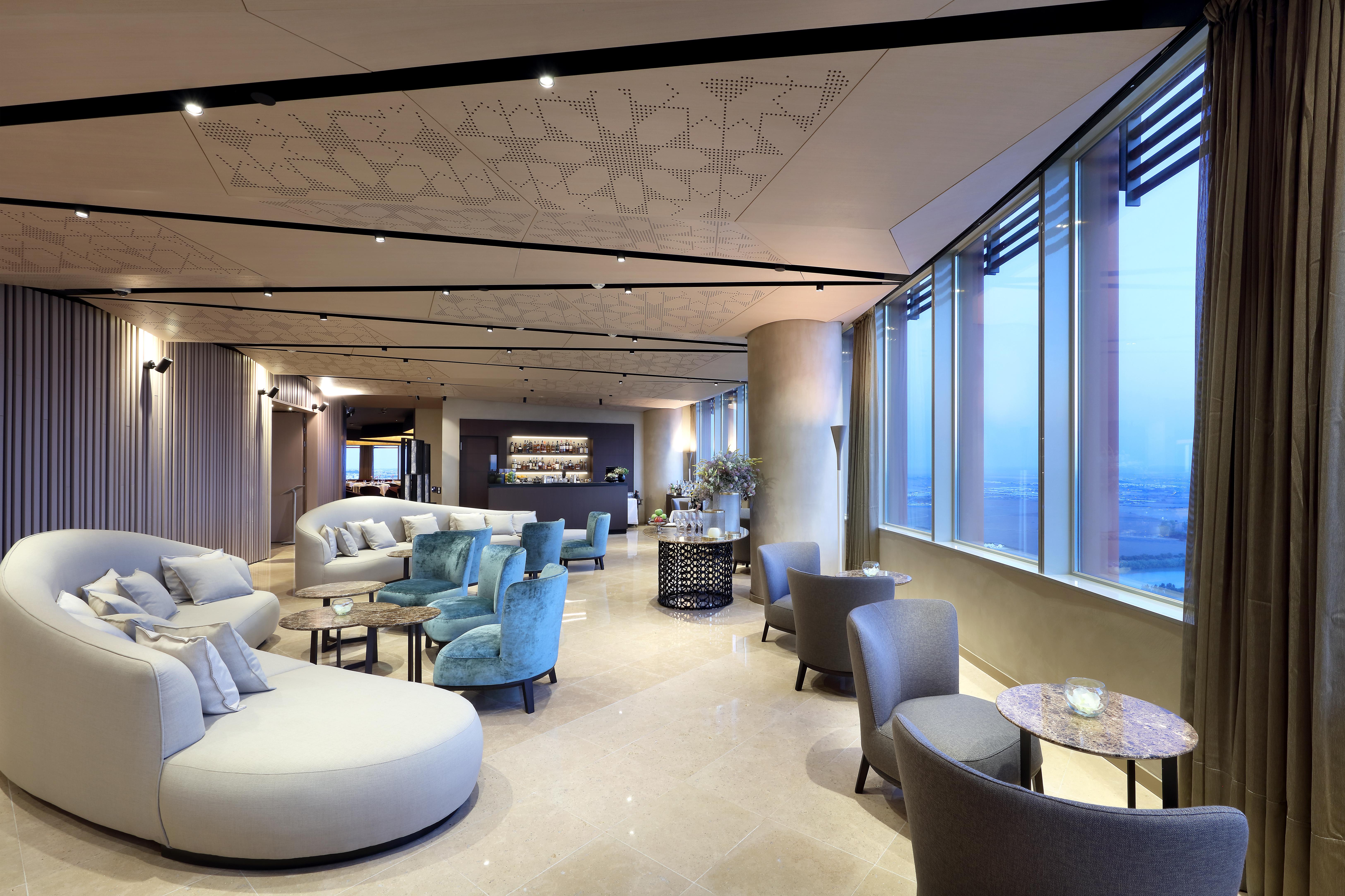 Eurostars Torre Sevilla Exterior foto The photo showcases a modern and stylish interior space, likely a lounge or waiting area. It features a combination of comfortable seating options, including curved white sofas and armchairs in light blue and gray tones. Large windows allow natural l