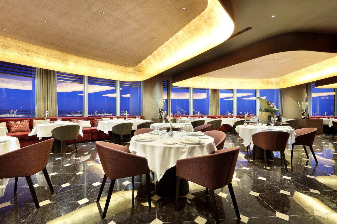 Eurostars Torre Sevilla Exterior foto The photo shows an elegant restaurant interior. It features modern decor with a sophisticated ambiance, including round tables covered with white tablecloths. The seating consists of stylish chairs, and large windows provide a view of the outside, li