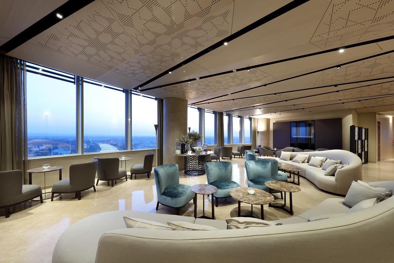 Eurostars Torre Sevilla Exterior foto The photo shows a modern, elegantly designed lounge or lobby area. It features large windows that provide expansive views of the landscape outside, allowing natural light to fill the space. The interior design includes a combination of soft, curved f