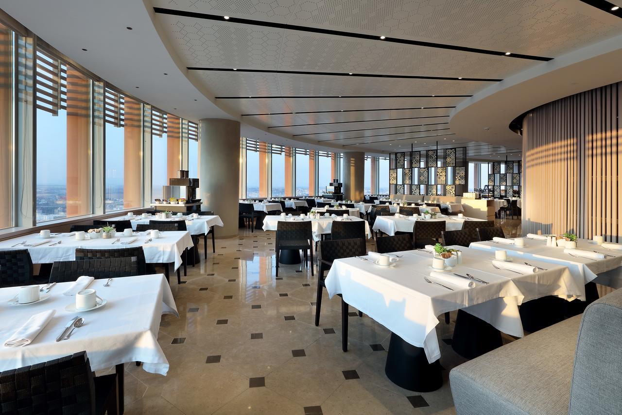 Eurostars Torre Sevilla Exterior foto The photo shows an elegant restaurant interior with a modern design. The space includes several tables, each set with white tablecloths and dishware. The restaurant features large windows that offer a panoramic view, allowing natural light to flood t
