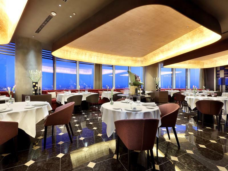 Eurostars Torre Sevilla Exterior foto The photo depicts a modern, upscale restaurant with an elegant interior design. The dining area features round tables, each set with white tablecloths and elegant dishware, indicating a fine dining atmosphere. The walls are adorned with large windows
