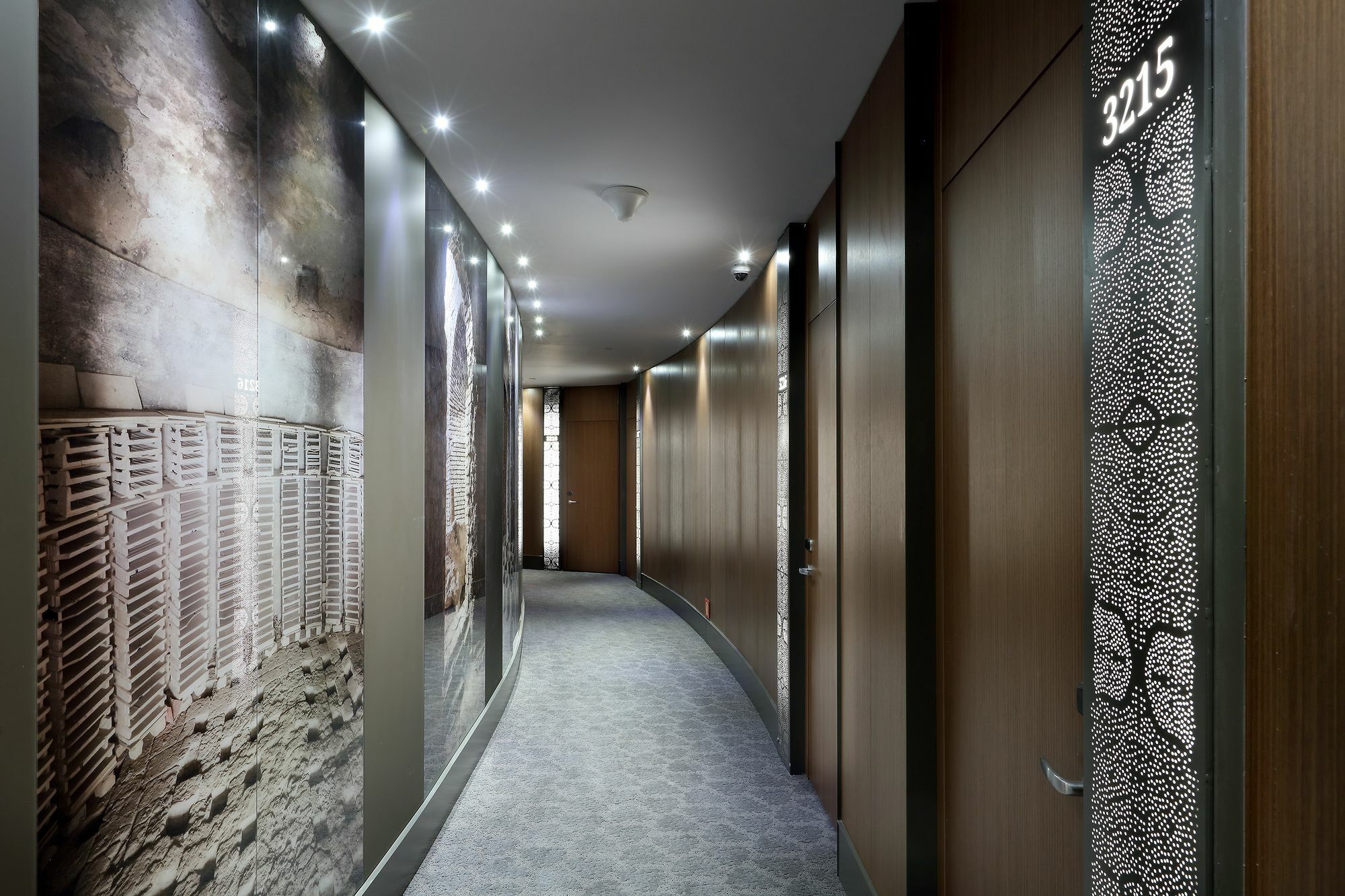 Eurostars Torre Sevilla Exterior foto The photo shows a modern hotel corridor with a curved design. The walls are adorned with large, artistic wall coverings featuring abstract and patterned designs. Soft lighting is embedded in the ceiling, creating a warm ambiance. The doors to guest r