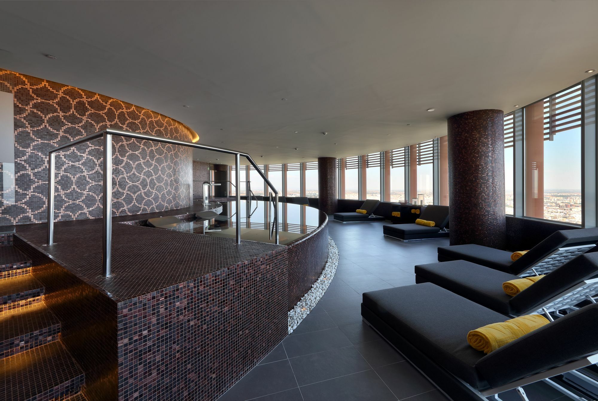 Eurostars Torre Sevilla Exterior foto The photo shows a modern spa or relaxation area with large windows that provide a panoramic view. The interior features a stylish design, highlighted by smooth, dark tiles and elegant stonework. There's a curved seating area with lounge chairs, accen
