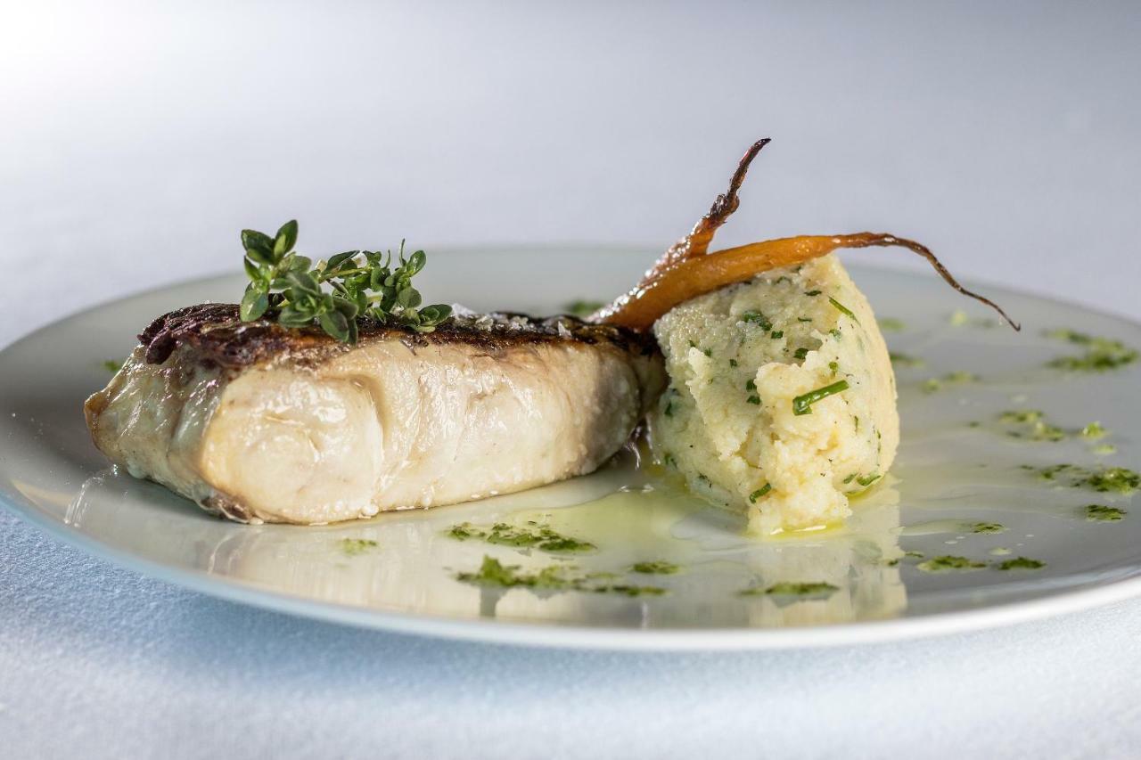Eurostars Torre Sevilla Exterior foto The photo shows a plate of food featuring a piece of cooked fish, which appears to be topped with fresh herbs, possibly thyme. Next to the fish, there is a serving of mashed potatoes that has a creamy texture and is garnished with herbs. Additionally