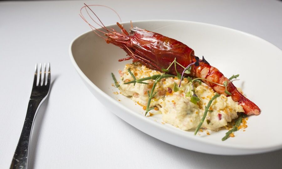 Eurostars Torre Sevilla Exterior foto The photo features a gourmet dish served in a white, oval bowl. It includes a large, grilled shrimp resting on a bed of creamy, textured food, likely a type of risotto or puree, which appears to include bits of vegetables. The dish is garnished with 